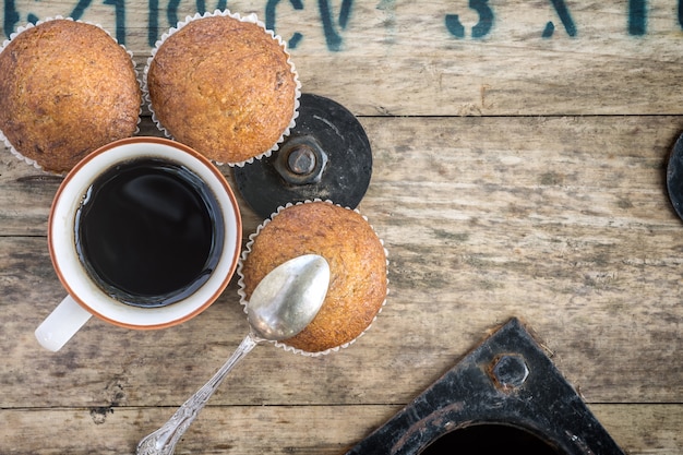 Heißer Kaffee und Bananen-Cupcake auf hölzernen Rollenstromkabel.