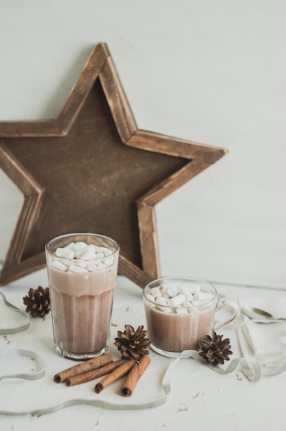 Heißer Kakao mit Marshmallows. Dekorationen mit Zimt, Tannenzapfen und weißen Servietten.