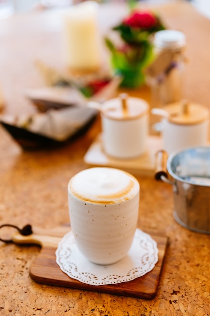 Heißer Latte diente in der keramischen Schale auf hölzerner Platte. Glatter weißer und brauner Schaum.