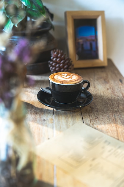 Heißer Milchcappuccinokaffee in der schwarzen Schale auf Holztisch mit Kopienraum