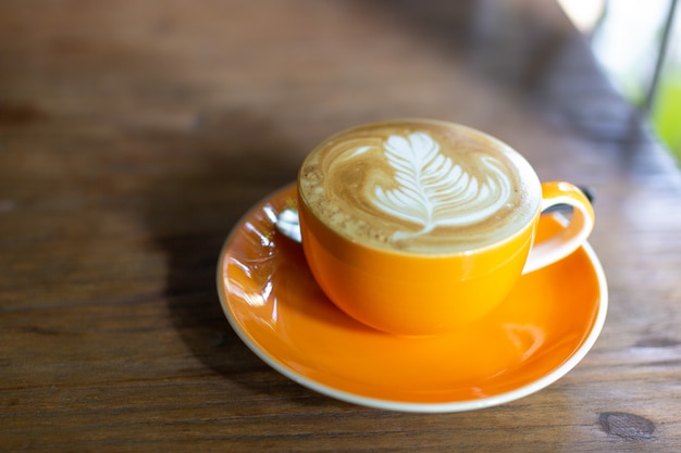Heißer Milchkaffee mit spätem Kunst auf Spitzenisolat auf Holztisch