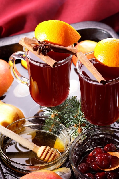 Heißer roter Glühwein Bienenhonig Scheiben Orangen und Gewürze auf dunklem Hintergrund Weihnachtsdekoration mit Fichtenzweigen und einer roten Serviette