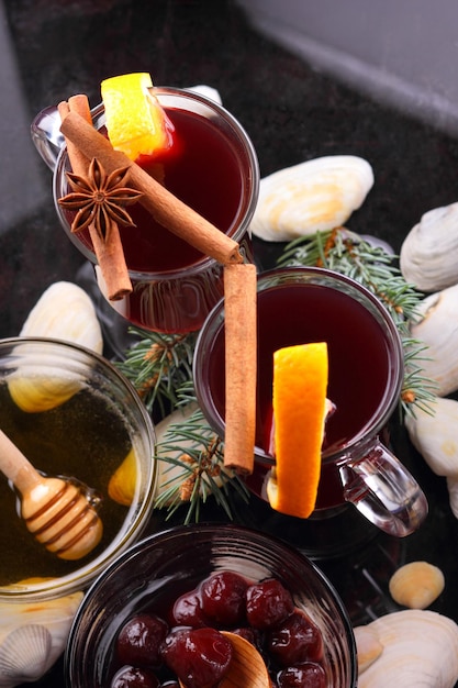 Heißer roter Glühwein Bienenhonig Scheiben von Orangen und Gewürzen auf dunklem Hintergrund Weihnachtsdekoration mit Fichtenzweigen Closeup