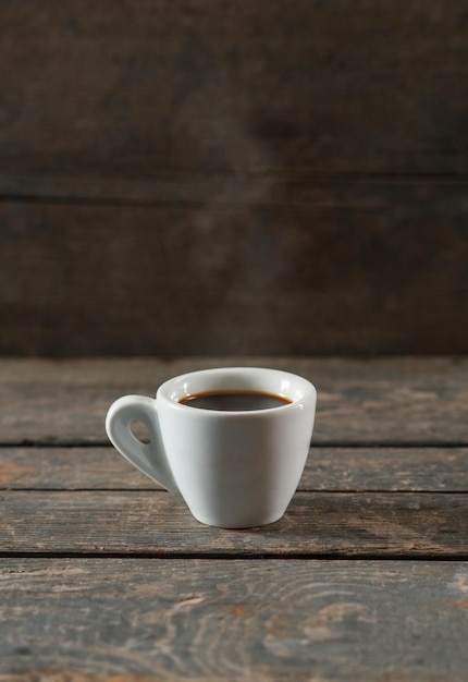 Heißer schwarzer Kaffee oder Espresso in weißer Keramiktasse auf hölzernem Texturhintergrund mit Dampf