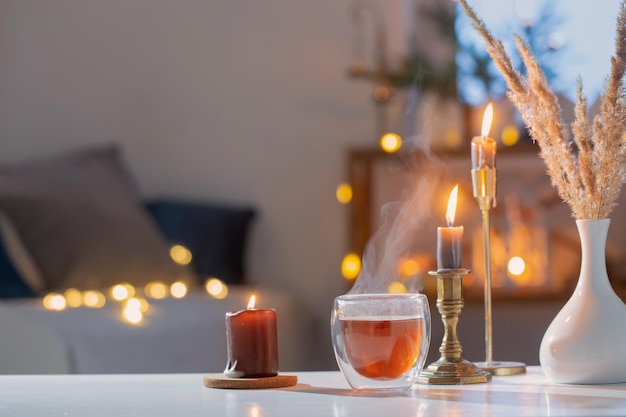 Heißer Tee im Thermoglas mit Weihnachtsdekor und brennenden Kerzen zu Hause