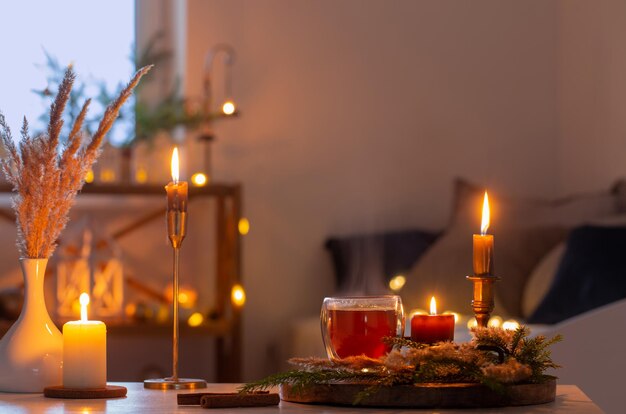 Heißer Tee im Thermoglas mit Weihnachtsdekoration und brennenden Kerzen zu Hause