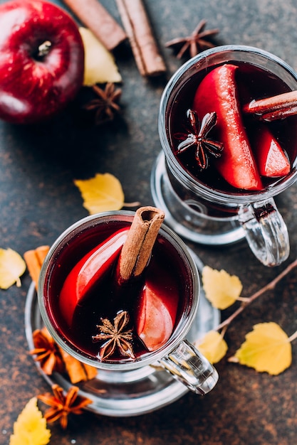 Heißes Fallgetränk des Glühweins mit Zitrusfrüchten, Apfel und Gewürzen im Glas auf dunklem Beton