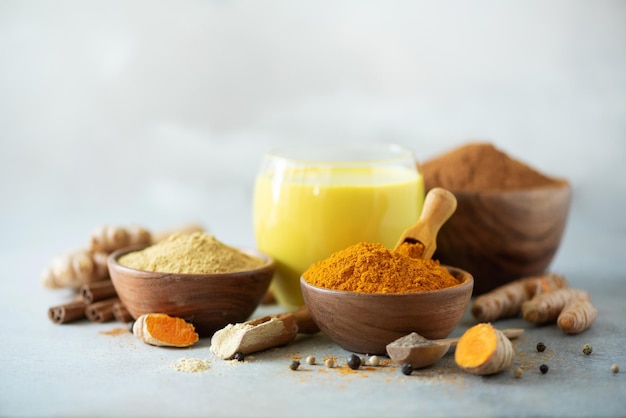 Heißes gesundes Getränk Kurkuma-Latte goldene Milch mit Kurkuma-Wurzel-Ingwer-Pulver schwarzer Pfeffer auf grauem Hintergrund Kopieren Sie Platz Gewürze für die ayurvedische Behandlung Konzept der alternativen Medizin