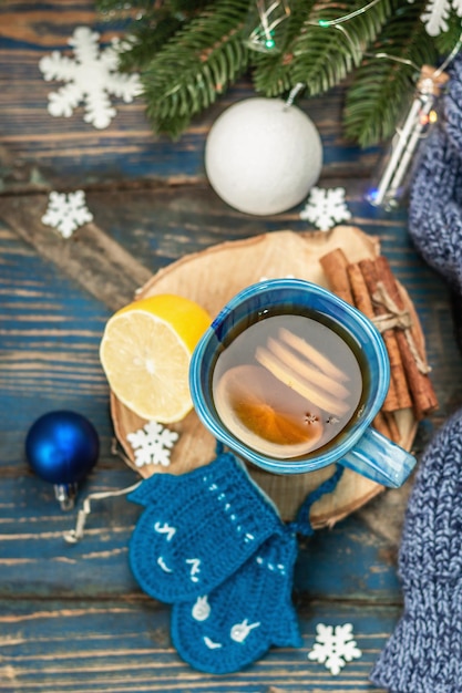 Heißes Getränk mit gehäkelten lustigen Fäustlingen. Traditionelles Winterdekor, Tannenzweige, Schneeflocken. Festliche saisonale Anordnung in Blautönen, alter Holzhintergrund, Draufsicht