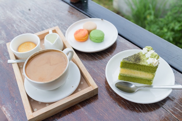 Heißes Kaffeefrühstücksset mit Kuchen des grünen Tees und frischer Makrone im gemütlichen Café im Freien