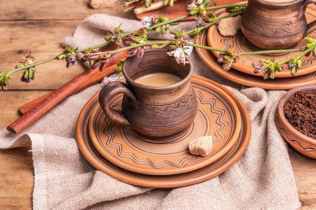 Heißes koffeinfreies natürliches Chicorée-Getränk in Keramikbechern auf einem Holztisch. Gesunder alternativer Ersatz für Kaffee, Koffein. Blaue Zichorienblüten, frische Wurzeln, Nahaufnahme