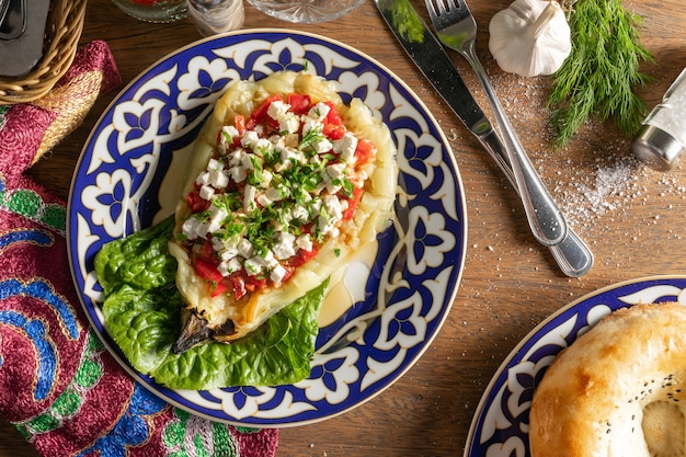 Heißes vegetarisches Gericht aus gegrillten Auberginen, gefüllt mit Fetaki-Käse und Baku-Tomaten, gewürzt mit Knoblauchsauce und Sojasauce in einem Teller mit einem traditionellen usbekischen Muster.