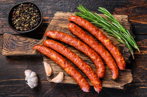 Heißgeräucherte Würste mit Zugabe von frischen aromatischen Kräutern und Gewürzen. Dunkler hölzerner Hintergrund. Ansicht von oben.