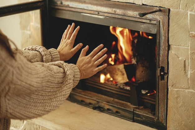 Heizhaus im Winter mit Holzofen Frau wärmt die Hände am brennenden Kamin auf