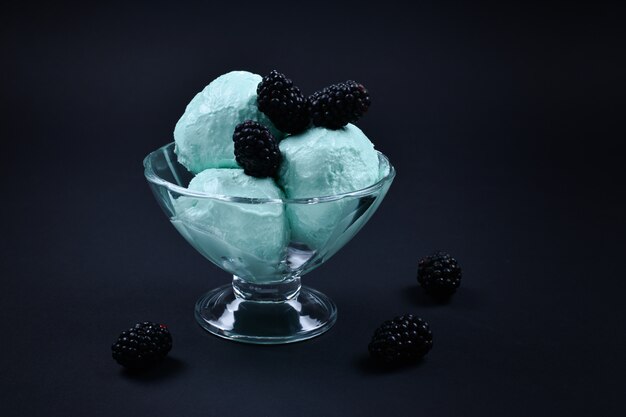 Helado azul en copa con bayas sobre fondo negro.