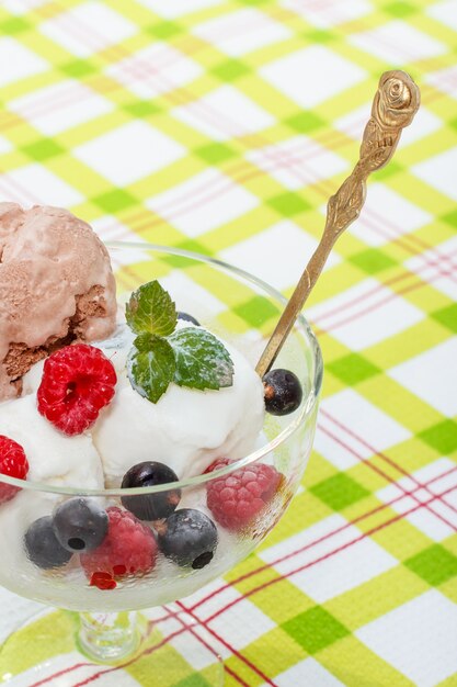 Helado blanco y chocolate en un vaso con frambuesa y grosellas y hojas de menta en una servilleta a cuadros