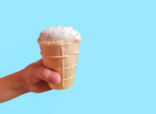 Helado blanco fresco en taza de galleta en la mano del niño sobre fondo azul.