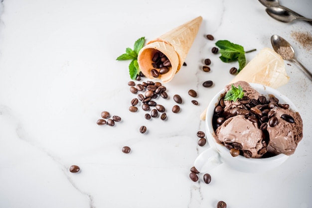 Helado de café casero, servido con granos de café y hojas de menta, con conos de helado y cucharas en la imagen. Fondo de mármol blanco