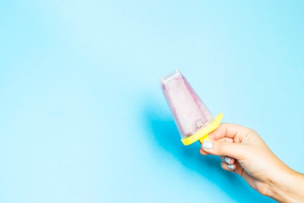 Helado casero de bayas en forma plástica en una mano femenina sobre un fondo azul