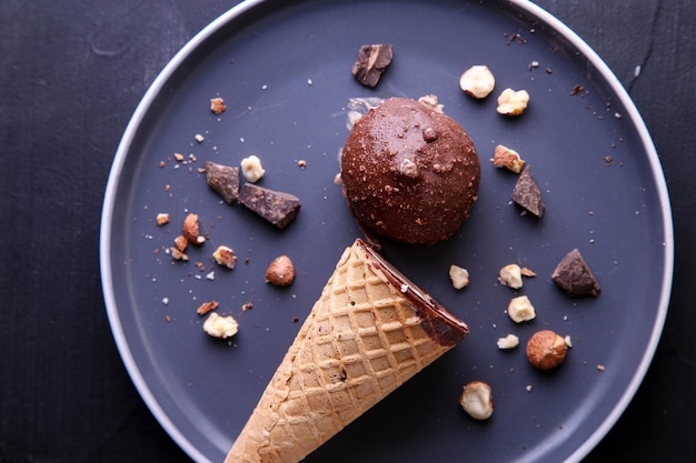 Helado de chocolate con avellanas en cono sobre una placa oscura