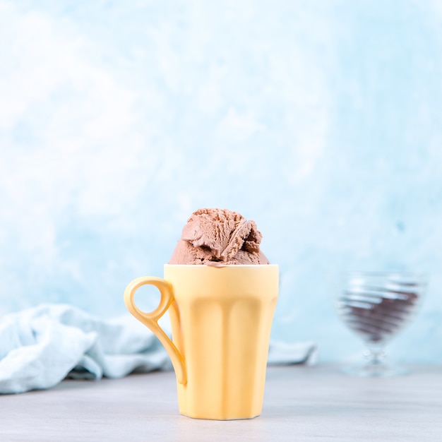 Foto helado de chocolate marrón en una taza amarilla normal, sobre azul.