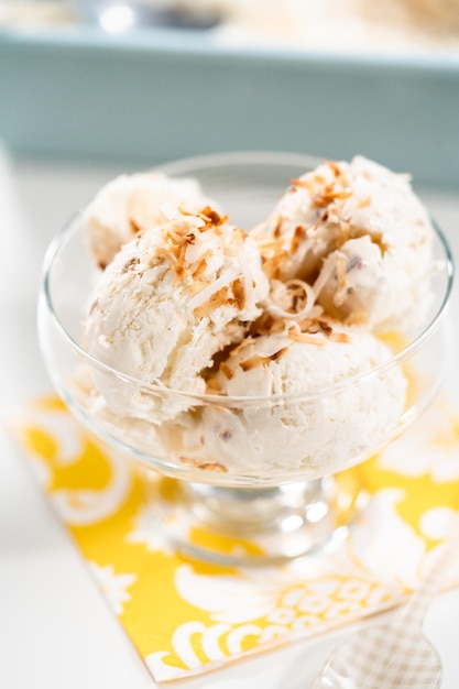 Helado de coco casero adornado con hojuelas de coco tostado en un tazón de vidrio para helado.