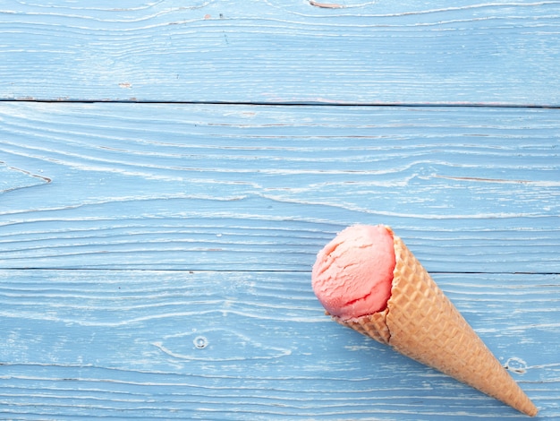 Helado de color rosa en un cono de galleta sobre un fondo azul de madera Vista superior espacio de copia