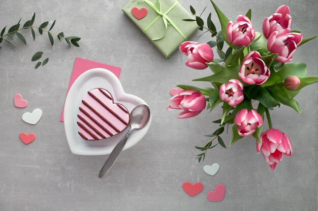 Helado de corazón rosa en plato de cerámica y ramo de tulipanes rosados