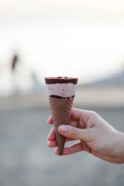 Helado de crema con chocolate en un primer plano de cono de galleta en la mano