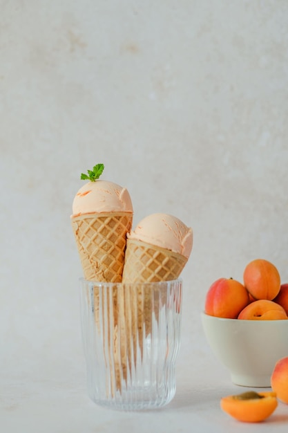 Helado cremoso de albaricoque vegano en el cuerno en un vaso, peinando hojas de menta encima.