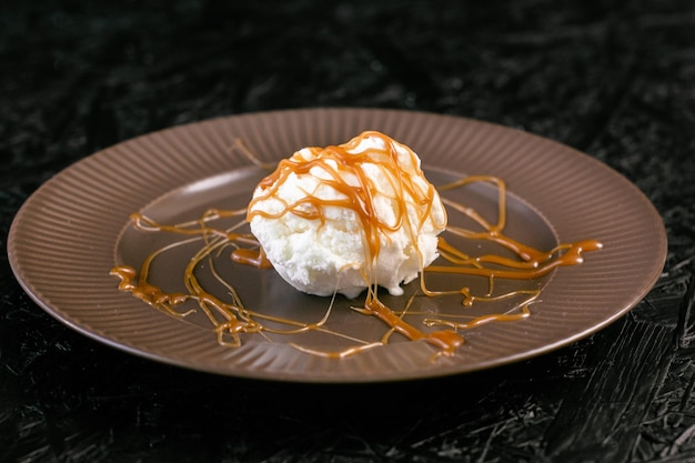 Helado cremoso con caramelo en un plato sobre un fondo oscuro.