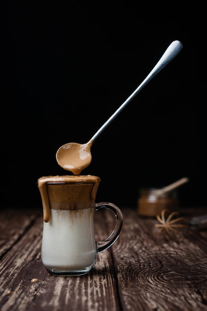 Helado Dalgona Coffee, un moderno café batido cremoso y esponjoso sobre una mesa de madera. Levitando la cuchara con la espuma. Primer plano, vista vertical.