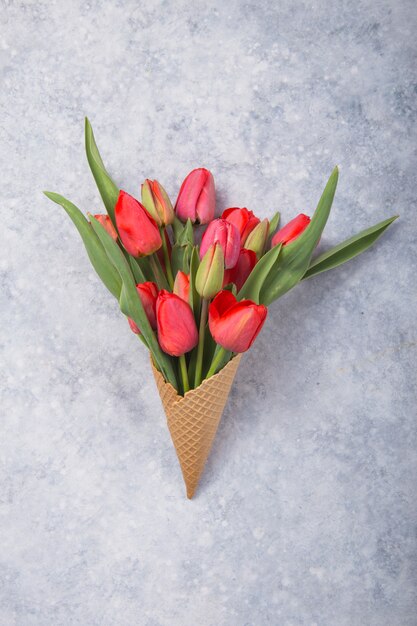 Helado de flores de tulipán rojo en cono de waffle en vista superior de mesa de concreto en estilo plano.