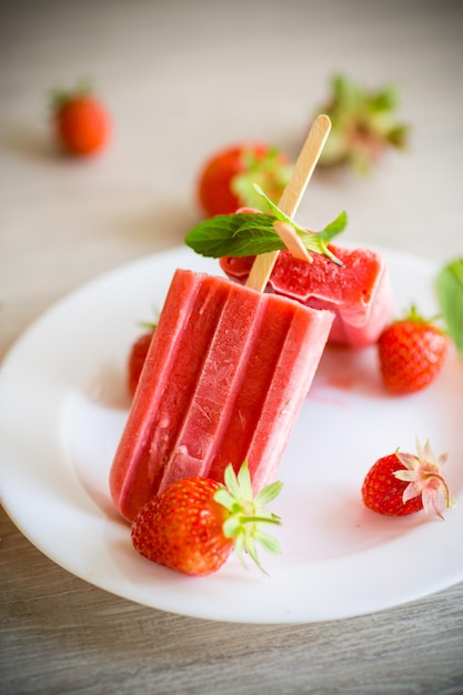 Helado de fresa casero en un palo hecho de fresas frescas en un plato sobre una mesa de madera