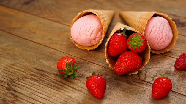 Helado de fresa en cono de galleta. Frutos rojos y bolas de helado sobre un fondo de madera.