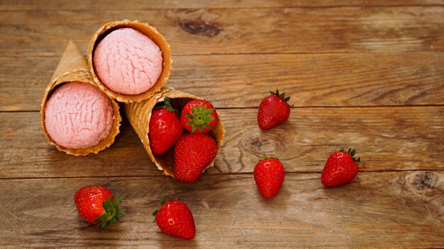 Helado de fresa en cono de galleta. Frutos rojos y bolas de helado sobre un fondo de madera.