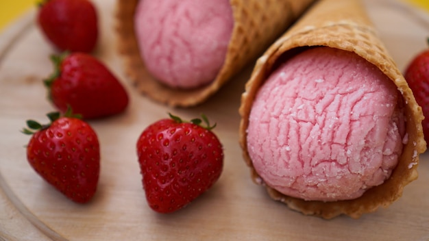 Helado de fresa en cono de galleta. Frutos rojos y bolas de helado sobre un fondo de madera.