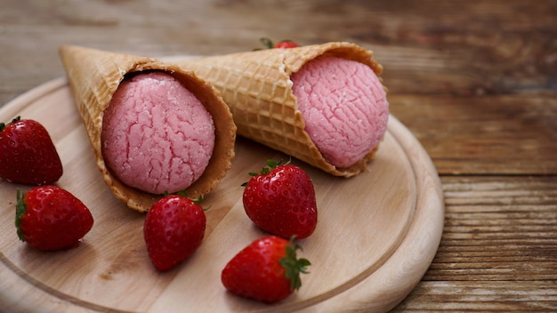 Helado de fresa en cono de galleta. Frutos rojos y bolas de helado sobre un fondo de madera.