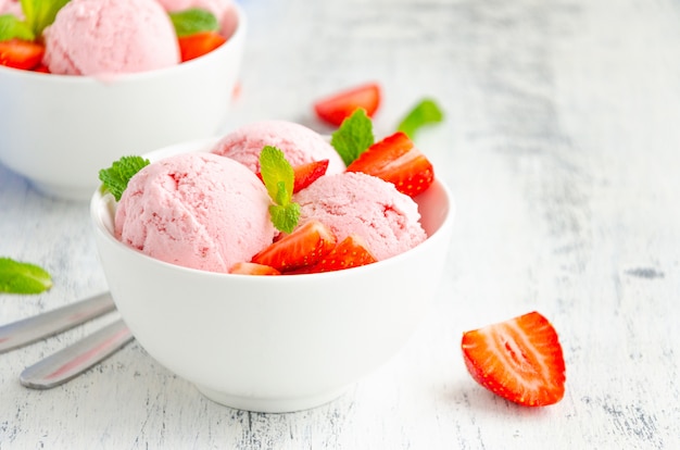 Helado de fresa en un recipiente con fresas frescas y menta sobre un fondo de madera. Copie el espacio.