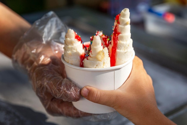 Helado de frutas en un vaso de papel en la calle El vendedor pasa el postre al niño Primer plano