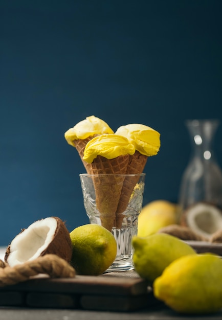 Foto helado de limón amarillo en un cuerno de waffle sobre una mesa de madera y azul oscuro. helado de coco y frutas.