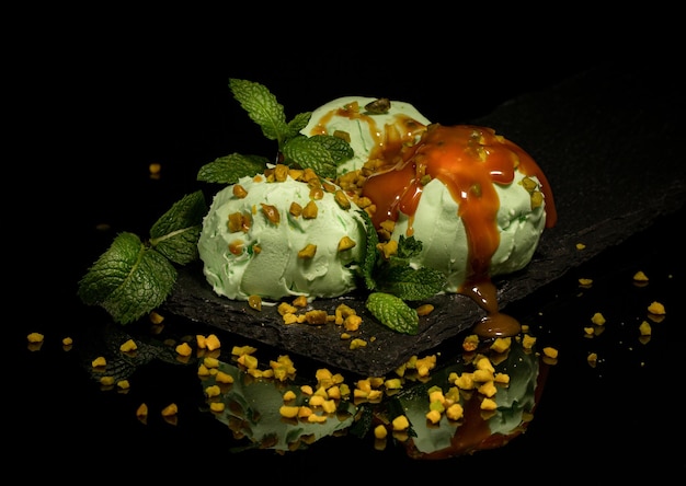 helado de pistacho, con glaseado de caramelo, menta, nueces, sobre una pizarra, vidrio negro