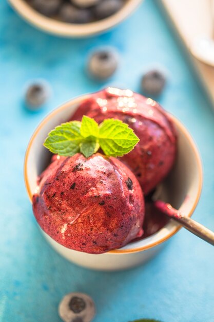 Foto helado de plátano vegano casero o helado con arándanos en un recipiente sobre fondo azul. postre saludable.