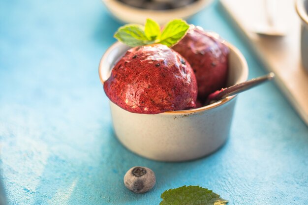 Helado de plátano vegano casero o helado con arándanos en un recipiente sobre fondo azul. Postre saludable.