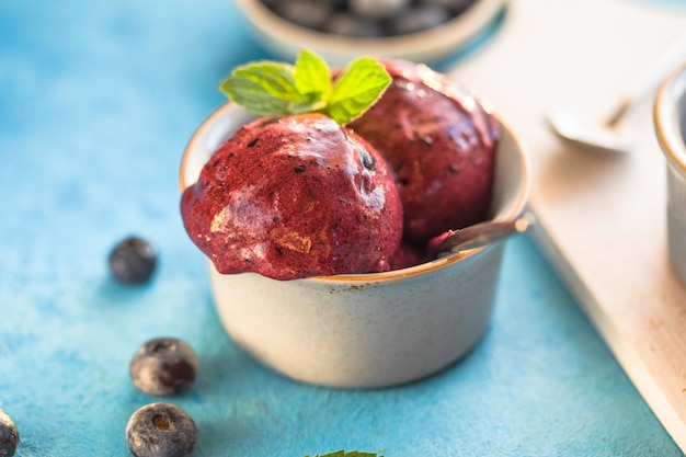 Helado de plátano vegano casero o helado con arándanos en un recipiente sobre fondo azul. Postre saludable.