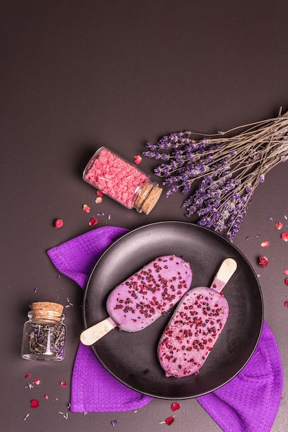 Helado con sabor a lavanda. Ramo de flores, azúcar rosa, pétalos de rosa. Fondo de hormigón de piedra negra, vista superior