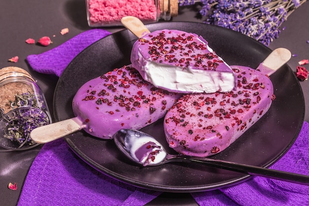 Helado con sabor a lavanda. Ramo de flores, azúcar rosa, pétalos de rosa. Luz dura de moda, sombra oscura. Fondo de hormigón de piedra negra, espacio de copia