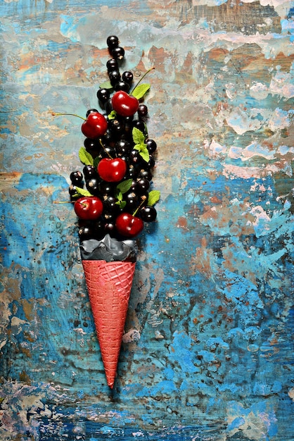 Helado en taza de gofre con grosellas negras, cerezas maduras y hojas de menta fresca