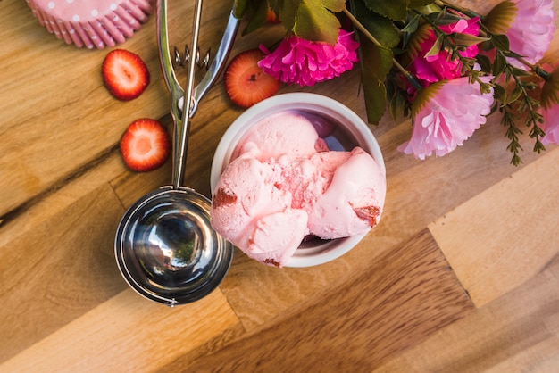 Helado en un tazón cerca de la cucharada con rodajas de bayas frescas y flores rosadas