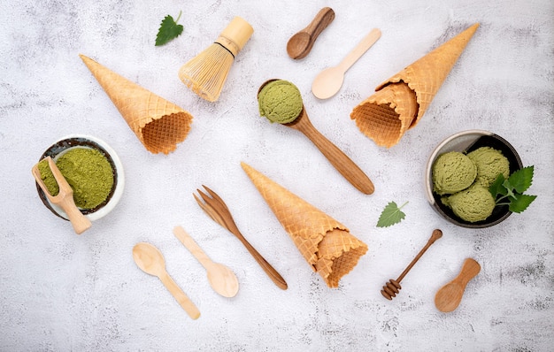 Helado de té verde matcha con cono de galleta y hojas de menta sobre fondo de piedra blanca.